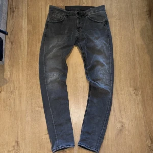Grå jeans från Dondup, storlek 33 - Snygga grå jeans från dondup med tvättad look och diskreta slitningar på benen. Modellen har raka ben och klassiska fem fickor. Bakfickorna har unik broderad detalj och en svart patch med vita ögon. Perfekta för dig som gillar streetwear med edge.
