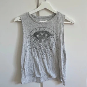 Grå linnetopp Abercrombie & Fitch XS - Säljer en grå ärmlös linnetopp från Abercrombie & Fitch i storlek XS. Toppen har ett coolt tryck med örn och texten 'Beauty is a state of mind' framtill. Mjuk och tunn bomull, perfekt till jeans eller shorts.