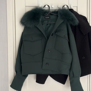 Mörkgrön jacka med pälskrage från Meotine - Säljer en mörkgrön, croppad jacka från Meotine med stor fluffig pälskrage. Jackan har två stora bröstfickor med lock, knäppning framtill och breda muddar vid ärmsluten. Perfekt för dig som vill sticka ut med en cool och trendig look. Dust bag medföljes💕