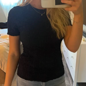 Marinblå ribbad topp med kort ärm - En marinblå topp med ribbad struktur och korta ärmar. Modellen är figurnära och har en enkel, rund halsringning. Perfekt att matcha med jeans eller kjol för en clean look.