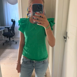 Grön volangblus från Newyorker  - Snygg grön blus från Newyorker med volangdetaljer på axlarna. Använd några gånger men är fortfarande i mycket bra skick