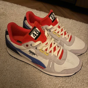 Puma RX 737 sneakers i vitt och rött - Säljer ett par Puma RX 737 sneakers med vit mesh och mockadetaljer, röda mesh-tungor och innersidor, blå och röda detaljer på sidorna samt gula accenter vid snörningen. Skorna har svart yttersula och klassisk Puma-logga på hälen. Nypris 1200 kr och dom är iprincip aldrig använda. 