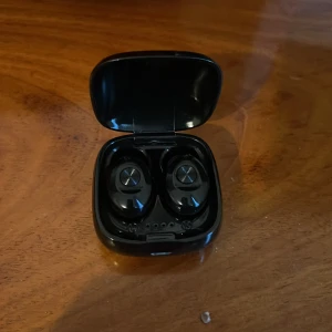 Svarta trådlösa hörlurar med laddningsetui - Snygga svarta trådlösa hörlurar med laddningsetui. Kompakt design, touchkontroller på öronsnäckorna. Hörlurarna och etuiet ser ut att vara i gott skick utan synliga repor eller skador. Perfekt för musik, samtal och träning.