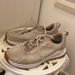 Beige Nike sneakers i mocka - Snygga Nike Rivah sneakers i beige mocka med vita och bruna sulor. Skorna har minimalistisk design, rund tå och snörning framtill. Perfekta för dig som gillar stilrena och bekväma sneakers med en modern touch. !skorna saknar sulor! 