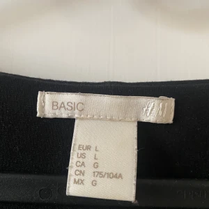 Svart enkel klänning från H&M Basic - Svart, stilren klänning från H&M Basic i figursydd modell med rund halsringning och långa ärmar. Perfekt för dig som gillar minimalistisk stil och vill ha något bekvämt och enkelt. Tillverkad i mjukt material som känns skönt mot huden. Ovan knä längd.