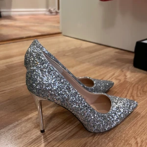 Glittriga silverpumps med spetsig tå - Säljer ett par riktigt snygga pumps från BIG TREE i silver med glittrig yta. Skorna har spetsig tå och hög klack i metallic. Aldrig använda i st 37🩶