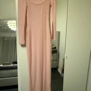Långärmad ribbad rosa maxiklänning - Supersnygg långärmad maxiklänning i ljusrosa med ribbad struktur. Klänningen har rundad urringning och är figurnära med långa ärmar. Perfekt för dig som gillar en stilren och feminin look.