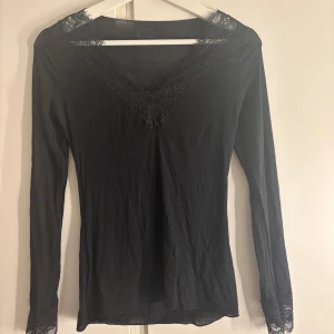 Svart långärmad topp med spets Intimissimi - Svart långärmad topp från Intimissimi . V-ringad med fina spetsdetaljer vid halsringning och ärmslut. 
