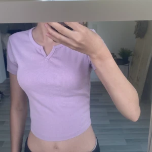 Ljuslila croppad topp från FB Sister - Säljer en ljuslila croppad topp från FB Sister i storlek XS. Toppen har korta ärmar, ribbad struktur och en snygg liten v-ringning framtill. 