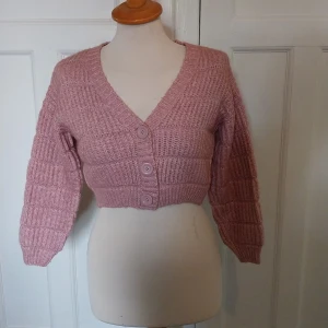 Rosa croppad kofta från Tally Weijl - Superfin croppad kofta i ljusrosa från Tally Weijl. Stickad med bred ribb, v-ringad och med tre stora knappar framtill. Perfekt till jeans eller kjol för en chill och trendig look.