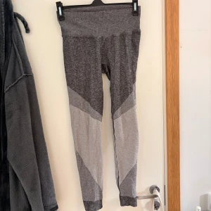 Gråmelerade leggings i M - Snygga gråmelerade leggings med hög midja och coola kontrastpaneler i ljusgrått. Perfekta för träning eller chill, med stretchigt och mjukt material som sitter skönt hela dagen.