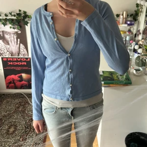 Ljusblå kofta från Saint Tropez - Supersöt ljusblå kofta från Saint Tropez i storlek S. Koftan har långa ärmar, rund halsringning och pärlknappar framtill. Perfekt att slänga över ett linne eller t-shirt för en chill look. Materialet känns mjukt och lätt, troligtvis bomull eller bomullsblandning.