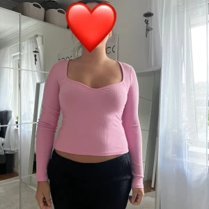 Rosa ribbad långärmad topp - Säljer en ljusrosa, ribbad långärmad topp med snygg v-ringning och croppad passform. Toppen har en figurnära siluett och är tillverkad i ett stretchigt material som sitter skönt på kroppen. Perfekt för dig som gillar en feminin och trendig stil.
