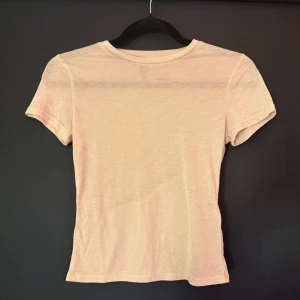 Rosa genomskinlig t-shirt från Divided - En enkel och stilren rosa t-shirt från Divided i storlek S. T-shirten har rund hals och korta ärmar, perfekt för en chill och avslappnad look. Materialet är mjukt och skönt bomull som känns nice mot huden. Passar dig som gillar basic och neutrala färger. NY UTAN PRISLAPP