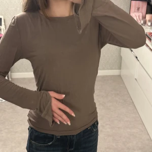 Brun långärmad topp med slits vid ärm - Säljer en brun långärmad topp med slits vid ärmsluten från Gina tricot. Modellen är enkel och har en rund halsringning. Materialet känns mjukt och lätt, perfekt för lager-på-lager eller som den är. Passformen är normal och toppen är stilren utan mönster eller tryck.