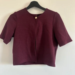 Vinröd kofta från Gina Tricot - Vinröd kofta från Gina Tricot med kort ärm och rund halsringning. Stängs med en guldfärgad knapp upptill. Väldigt bra skick och perfekt färg nu till hösten! 
