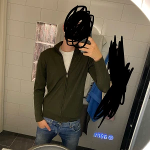 Oscar Jacobson - Säljer en stilren mörkgrön kofta från Oscar Jacobson i storlek M. Tröjan är stickad, har hel dragkedja framtill och hög krage. Perfekt för lager-på-lager och funkar lika bra till jeans som chinos. Hör av dig vid fler funderingar!