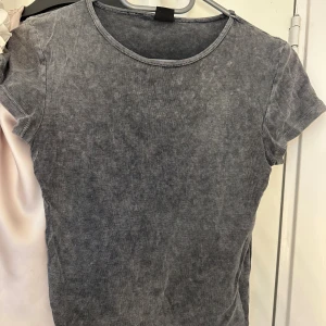 Grå t-shirt med tvättad look - Snygg grå t-shirt med tvättad effekt och rund hals. Modellen är klassisk med korta ärmar och har en mjuk, skön känsla. Perfekt för dig som gillar en enkel men cool stil. Passformen är normal och materialet känns som bomull.