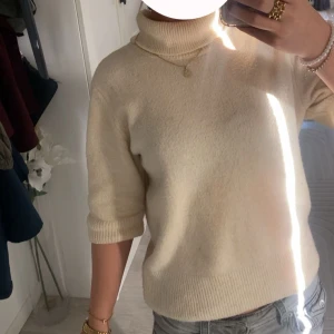 Beige polotröja i ullmix - Supermysig beige polotröja med ribbade muddar och halvlånga ärmar. Tröjan är stickad i mjuk ullmix och har en klassisk, lite loose passform. Perfelt till hösten. Lite nopprig men det går att lösa. Pris går att diskutera