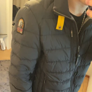 Svart pufferjacka från Parajumpers - Säljer en svart pufferjacka från Parajumpers med klassisk patch på ärmen och gul detalj vid kragen. Jackan har dragkedja framtill och två sidofickor med dragkedja. Perfekt för kyliga dagar och riktigt snygg till streetwear 100% äkta skriv vid funderingar den är helt utan defekter 