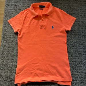Orange pikétröja från Ralph Lauren XS - Säljer en snygg orange pikétröja från Ralph Lauren i modellen The Skinny Polo. Tröjan har klassisk krage, korta ärmar och blå broderad logga på bröstet. Tillverkad i bomull och passar perfekt till vår och sommar.