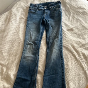 Blå bootcut jeans från H&M - Snygga blå bootcut jeans från H&M med låg midja och justerbar midja. Jeansen har klassisk femficksdesign och är tillverkade i ett stretchigt denimtyg som sitter skönt. Perfekta för dig som gillar en avslappnad men trendig look.