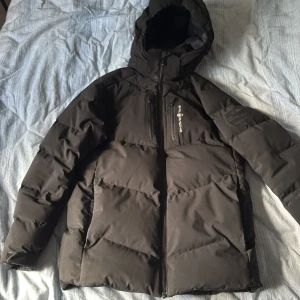 Svart Sail Racing jacka - Svart pufferjacka från Sail Racing med huva och dragkedja framtill. Jackan har två stora fickor på sidorna och en bröstficka med Sail Racing-logga. Hör av er om ni vill ha fler bilder och info😁