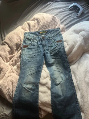 Blå jeans med broderade bakfickor - Säljer ett par unika jeans med snygg ”slitningar” och broderade detaljer på bakfickorna.de har en unik tvätt som ger en cool look. Perfekta för dig som vill sticka ut lite extra kanske! Köpta i Spanien, och är i storlek 27🫶🏻