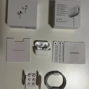 AirPods Pro 2 trådlösa hörlurar - Säljer ett par vita Apple AirPods Pro 2 med laddningsetui. Hörlurarna har in-ear design, silikonproppar och levereras med originalförpackning, extra öronproppar och laddningskabel. Perfekta för musik, samtal och brusreducering.
