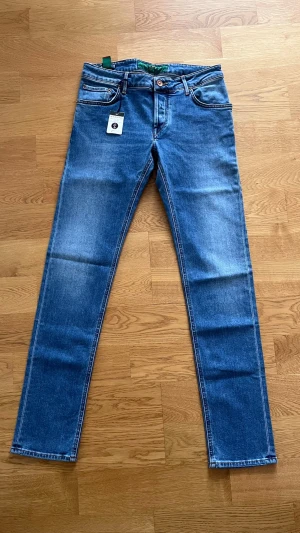 Blå  jeans från Handpicked - Säljer ett par klassiska blå jeans från Handpicked med raka ben och fem fickor. Jeansen har en snygg tvättad look, kontrastsömmar och patch bak i midjan. Tillverkade i mjuk bomullsdenim med stretch för extra komfort.