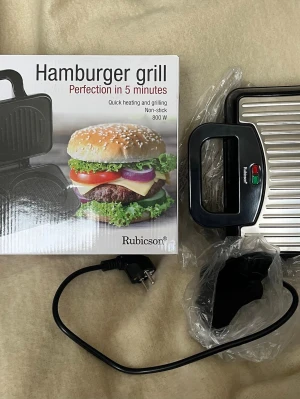 Hamburgergrill Rubicson 800W - Smidig hamburgergrill från Rubicson med non-stick yta och 800W effekt. Grillen har svart handtag och silverfärgad ovansida, perfekt för att snabbt grilla hamburgare hemma. Kommer med originalkartong och sladd. Använd en gång. Självklart väl rengjord. Kom ej till användning hos oss utan söker nu ett nytt ock kärleksfullt hem! ♥️