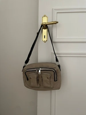Núnoo bag / axelremsväska - som ny!  - Säljer nu min Núnoo bag som jag köpte för ett gäng år sedan som knappt använts. Ser ut som ny i skicket. Har många fack och är mycket rymlig. Kommer i ett lite hårdare material (lite som jute) med svarta och silvriga detaljer. 