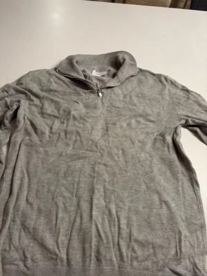 Grå halvzip tröja  - En stilren grå tröja med halv dragkedja och hög krage. Tröjan har långa ärmar och ribbade muddar vid ärmslut och nederkant. Perfekt för lager-på-lager och enkel att matcha med andra plagg. Knappt använd!
