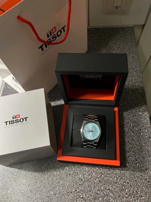 Tissot PRX klocka med blå urtavla - Snygg Tissot PRX klocka med stilren blå urtavla och silverfärgat armband i rostfritt stål. Klockan har en klassisk rund form och minimalistisk design, perfekt för dig som gillar en clean och modern look. Levereras i originalask.