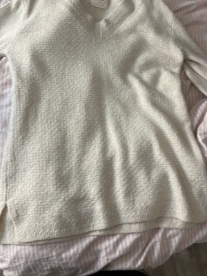 Beige stickad tröja med v-ringning - Mysig beige stickad tröja med v-ringad hals och långa ärmar. Tröjan har ribbstickade muddar vid ärmslut och nederkant, samt en avslappnad passform. Perfekt för lager på lager och enkel att matcha med olika stilar. Köpt i Spanien. 