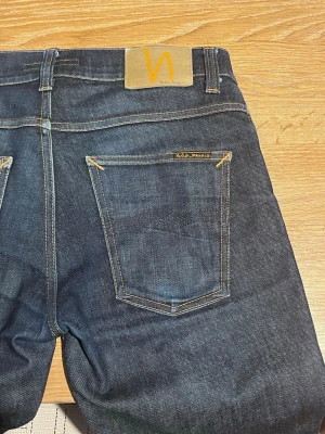Nudie Jeans - Nypris: 1600 kr.                                              Nudie jeans i modellen Grim tim Navy blue. Väldigt starkt tyg därav är jeansen fortfarande i väldigt bra skick, bortsett från slitagen som visas på bilderna, pga accessoarer som har expanderat tyget. 