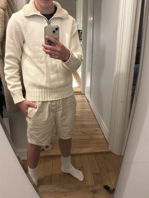 Offwhite stickad halfzip från Marc O'Polo - Snygg offwhite stickad tröja från Marc O'Polo med halv dragkedja och hög krage. Tröjan har ribbstickade muddar vid ärmslut och nederkant samt diskret logga vid höften. Perfekt för lager-på-lager och stilrena outfits.