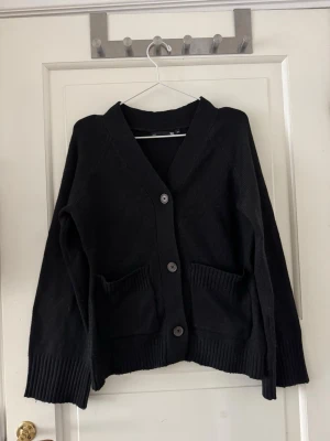 Figursydd stickad kofta - Stickad kofta ”Sabrina” från lager 157 i storlek XS men passar även S. Svart. Använd en gång och tvättad efter. Kan förekomma några noppror pga tvätt. 3% Ull och 97% polyester. Figursydd , v-ringad, vida ärmar. Skickar med en extra knapp. Inköpt för 200kr. 