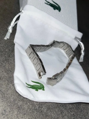 Lacoste armband - En härlig Lacoste armband jag fick av min faster som present. Jag vill sälja den då jag inte tar på mig smycken. Allt på bilden ingår. Pris går att diskuteras vid snabb affär.