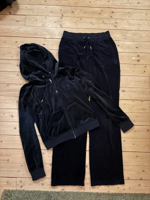 Mörkblått Juicy Couture set - Mysigt mörkblått velourset från Juicy Couture. Tröja i strl s, Byxor i Strl M. Med dragkedja och huva på tröjan samt broderad logga på bröstet. Byxorna har resårmidja med snörning och raka ben. 