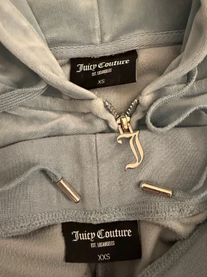 Juicy couture ljusblå  - Ett jättehärligt mjukiset från juicy couture i färgen ljusblå. Huvtröjan är i storlek xs och byxorna i xxs. De har använts men inga märkvärdiga tecken på det förutom ett lagat hål i luvan (se sista bilden). Nypris ca. 2000kr+🩵