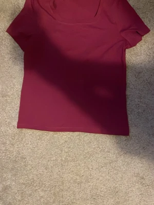 Mörkröd kortärmad topp - En enkel och stilren mörkröd topp med korta ärmar och rund halsringning. Perfekt att matcha med jeans eller kjol för en snygg look. Toppens material känns mjukt och stretchigt.