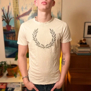 Vit Fred Perry t-shirt med logga - Snygg vit t-shirt från Fred Perry med den klassiska lagerkrans-loggan i grått på bröstet. T-shirten har rund hals och korta ärmar, perfekt för en clean och stilren look.