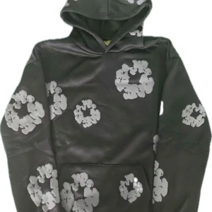 Denim tears hoodie - Snygg svart denim tears hoodie med gråa blommönster över hela tröjan. Hoodien har en klassisk huva och en stor magficka framtill. Perfekt för dig som vill sticka ut med en unik och trendig stil.