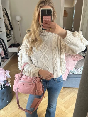 Vit/beige chunky stickad tröja med fransar - Säljer en vit /beige chunky stickad tröja med flätmönster och fransar längs ärmarna. Tröjan har hög hals och ribbade muddar. Perfekt för dig som gillar en mysig och trendig look till höst och vinter.