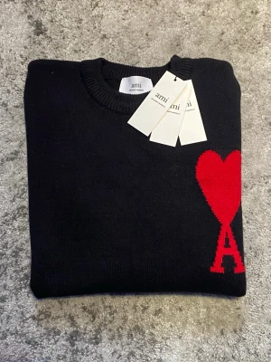 Svart Ami Paris tröja - Riktigt fet Ami tröja i svart med röd logga på bröstet. Tröjan är storlek S och skicket är mycket bra, utan  några defekter. Perfekt för dig som söker en stilren look med en gnutta elegans. Hör gärna av dig om funderingar som mått, pris, bilder etc. Så löser vi! 😁