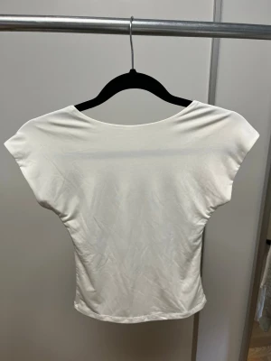 Vit croppad topp med öppen rygg - Säljer en vit croppad topp med öppen rygg och korta ärmar. Toppen har en enkel och clean look med rundad halsringning och är tillverkad i ett mjukt, stretchigt material som känns skönt mot huden. Perfekt för dig som gillar minimalistisk stil.