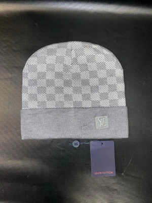 Grå mössa med rutmönster - Snygg grå mössa med klassiskt rutmönster och vikt kant. Loggan framtill på kanten. Perfekt accessoar för att lyfta din stil under kyliga dagar. Materialet känns mjukt och bekvämt mot huden.