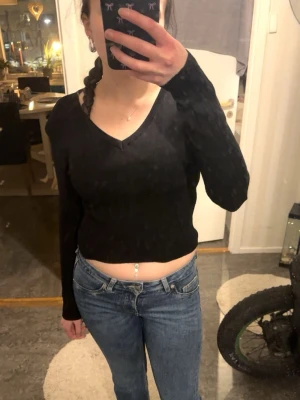 Svart croppad ribbad långärmad topp - Svart croppad topp med lång ärm och v-ringning. Tillverkad i ribbad bomullsmix som ger en skön och stretchig passform. Perfekt till jeans eller kjol för en enkel men snygg look.