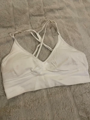 Vit sport-bh med korsade band - Säljer en vit sport-bh med smala, korsade axelband i ryggen. Materialet är stretchigt och mjukt, perfekt för träning eller chill. Denna bh är nästan som ny!
